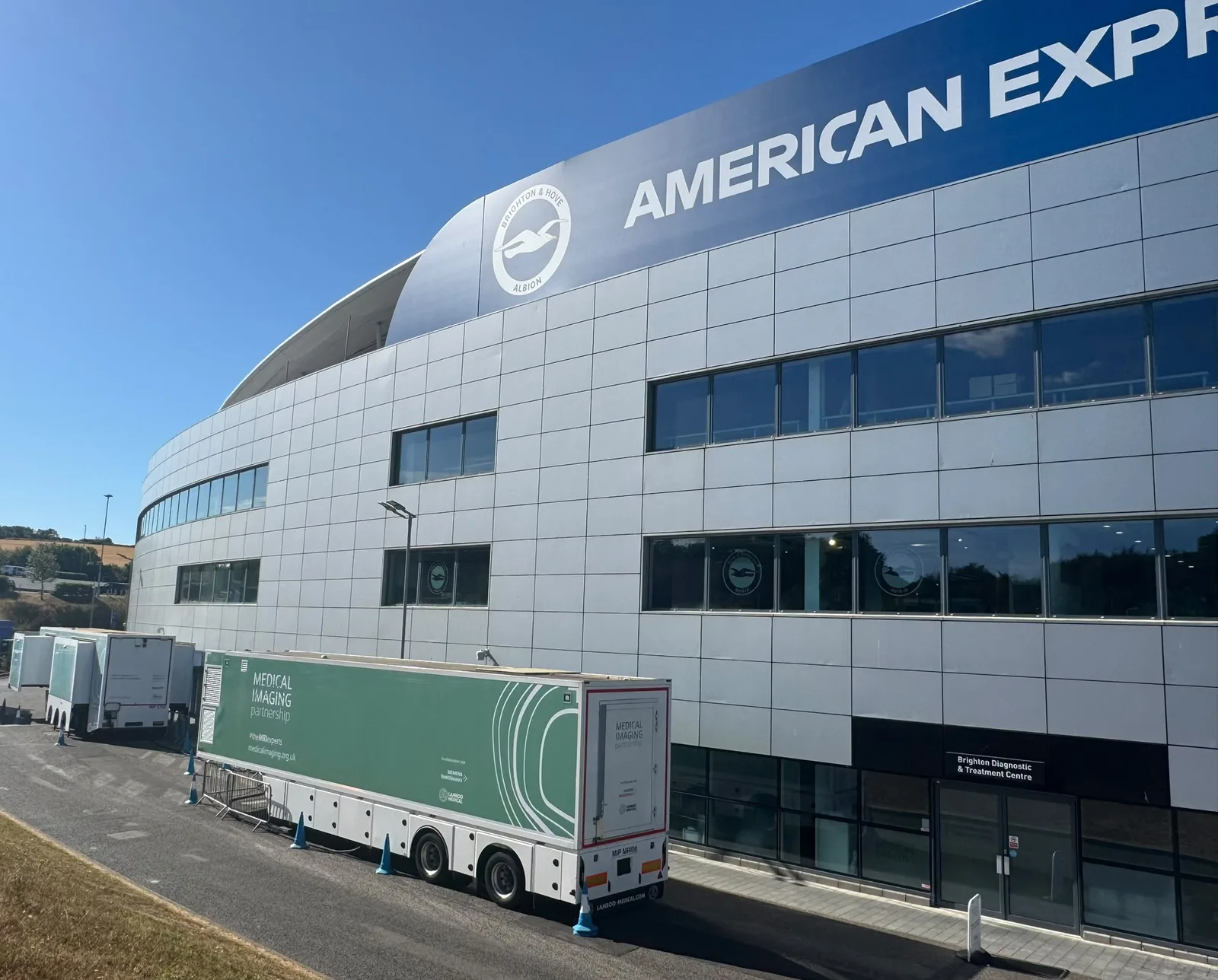 Medical Imaging Partnership mobile diagnostic units lined up beside the American Express Stadium, with the Brighton Diagnostic and Treatment Centre entrance to the right